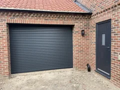 Anthracite roller garage door with a matching side door in a brick garage