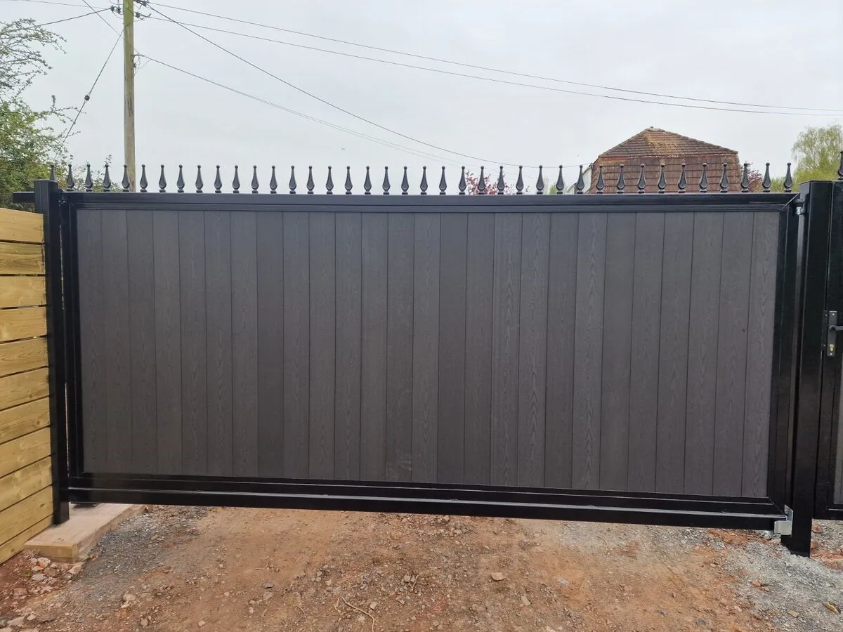 Grey sliding driveway gate with solid vertical infill between stone posts.