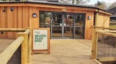 Glazed automatic entrance doors in a timber-clad shopfront, approached by a decked walkway.